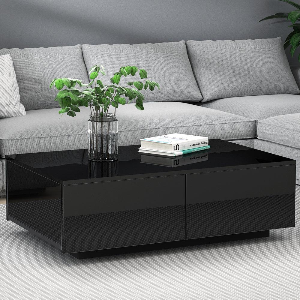 Modern black coffee table with glass top, books, and a plant, in front of a grey sofa.